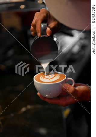 Professional male barista pouring a steamed milk into a coffee cup, making a latte art 91435596