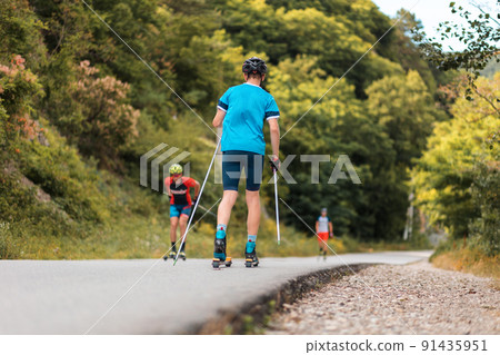Group of sportsmen training before the competition. View from the back. Biathlon ride on the roller skis with ski poles, in the helmet. Concept of sport and summer contest 91435951