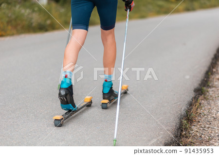 Legs of a biathlete athlete with ski poles, close-up. Concept of rollers ski and summer workout Legs of a biathlete athlete with ski poles, close-up. Concept of rollers ski and summer workout 91435953