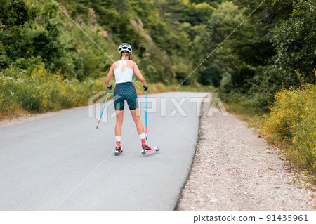 Athletic young woman training on the roller ski at country road, back view. Copy space. Concept of competition, biathlon, and summer workout Athletic young woman training on the roller ski at country road, back view. Copy space. Concept of competition, biathlon, and summer workout 91435961