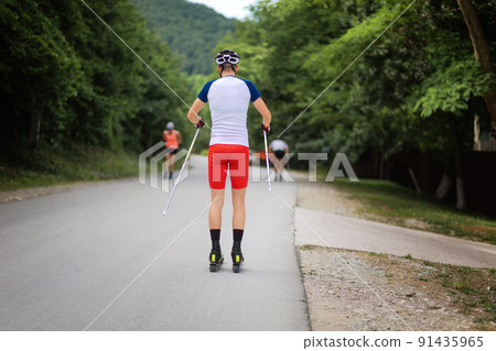 A group of athletes train before the competition. View from the back. Biathlon ride on the roller skis with ski poles, in the helmet. Concept of sport and summer contest A group of athletes train before the competition. View from the back. Biathlon ride on the roller skis with ski poles, in the helmet. Concept of sport and summer contest 91435965