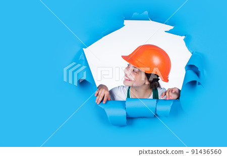 teen girl builder in protective helmet looking through blue background, architecture teen girl builder in protective helmet looking through blue background, architecture 91436560
