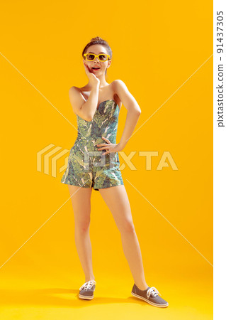 Full-length portrait of beautiful young girl posing isolated over yellow studio background. Emotive Full-length portrait of beautiful young girl posing isolated over yellow studio background. Emotive 91437305