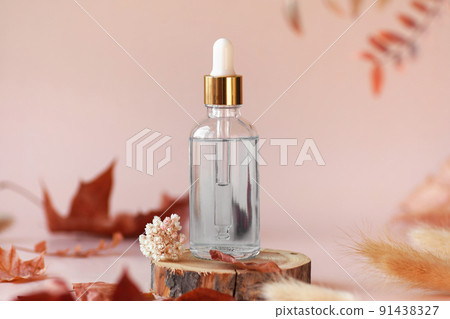 Transparent glass cosmetic dropper bottle standing on wooden disk with dry flowers and leaves on beige background. Autumn composition. Concept of natural and organic skincare products presentation 91438327