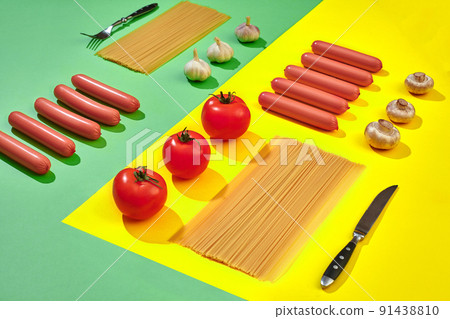 Sausages with tomatoes, mushrooms, spaghetti and garlic on a green and yellow minimal background. Flat lay. Top view. Sausages with tomatoes, mushrooms, spaghetti and garlic on a green and yellow minimal background. Flat lay. Top view. 91438810