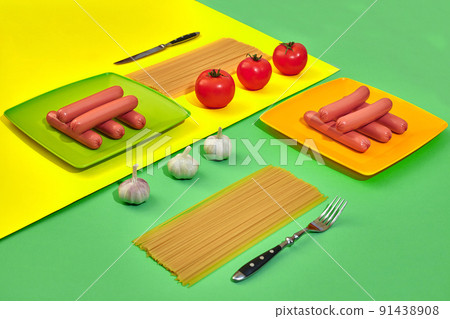 A lot of raw sausages on plate. On green and yellow background with pasta and vegetables, top view. A lot of raw sausages on plate. On green and yellow background with pasta and vegetables, top view. 91438908