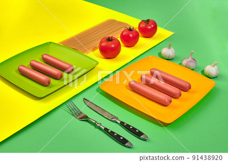 A lot of raw sausages on plate. On green and yellow background with pasta and vegetables, top view. A lot of raw sausages on plate. On green and yellow background with pasta and vegetables, top view. 91438920