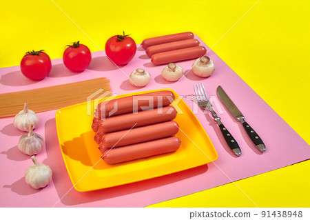 A lot of raw sausages on plate. On pink and yellow background with pasta and vegetables, top view. A lot of raw sausages on plate. On pink and yellow background with pasta and vegetables, top view. 91438948