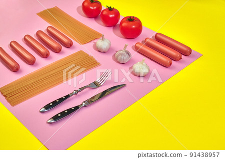A lot of raw sausages with pasta and vegetables on pink and yellow background, top view. A lot of raw sausages with pasta and vegetables on pink and yellow background, top view. 91438957