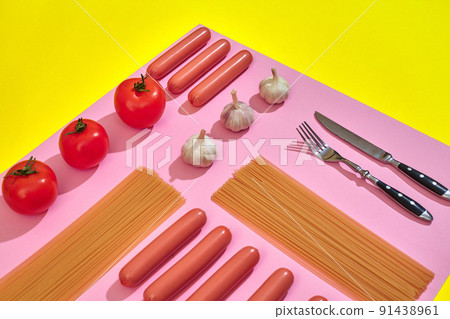 A lot of raw sausages with pasta and vegetables on pink and yellow background, top view. A lot of raw sausages with pasta and vegetables on pink and yellow background, top view. 91438961