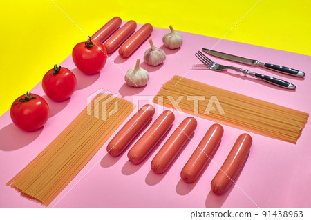 A lot of raw sausages with pasta and vegetables on pink and yellow background, top view. A lot of raw sausages with pasta and vegetables on pink and yellow background, top view. 91438963