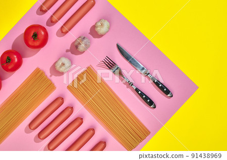 Sausages with tomatoes, spaghetti and garlic on a yellow and pink minimal background. Flat lay. Top view. Sausages with tomatoes, spaghetti and garlic on a yellow and pink minimal background. Flat lay. Top view. 91438969