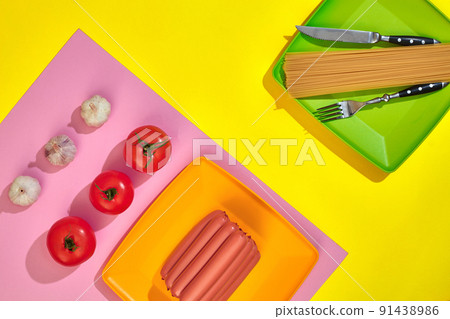 A lot of raw sausages on plate. On yellow background with pasta and vegetables, top view. 91438986