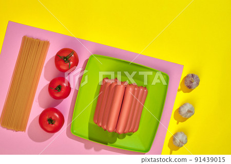 A lot of raw sausages on plate. On yellow background with pasta and vegetables, top view. 91439015