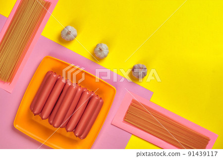 Sausages with spaghetti and garlic on a yellow and pink minimal background. Flat lay. Top view. Sausages with spaghetti and garlic on a yellow and pink minimal background. Flat lay. Top view. 91439117