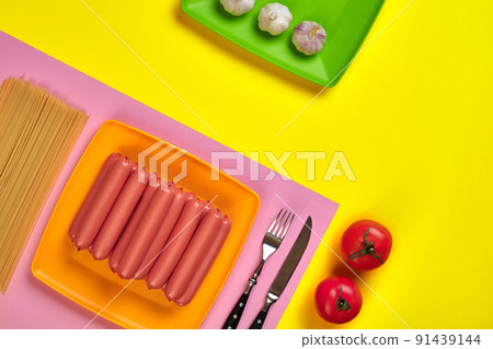 Sausages with tomatoes, spaghetti and garlic on a yellow and pink minimal background. Flat lay. Top view. 91439144