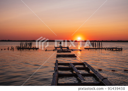 Beautiful red and orange sunset over the sea. The sun goes down over the sea. A flock of cormorants sits on a old sea pier in orange sunset light 91439438