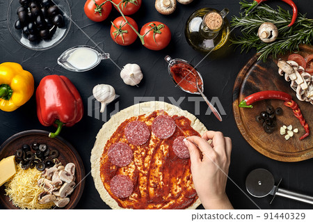 Hands of baker adding ingredients into pizza during pizza preparation at kitchen 91440329