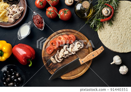 Cutting wooden board with traditional pizza preparation ingredients: cheese, tomatoes, sauce, mushrooms, olive oil, pepper, spices. Black texture table background Cutting wooden board with traditional pizza preparation ingredients: cheese, tomatoes, sauce, mushrooms, olive oil, pepper, spices. Black texture table background 91440351