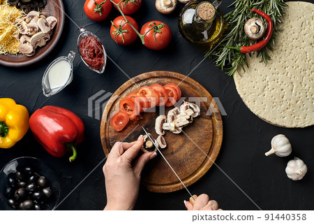 Female hand cut mushrooms and tomatoes on wooden board on kitchen table, around lie ingredients for pizza: vegetables, cheese and spices. Female hand cut mushrooms and tomatoes on wooden board on kitchen table, around lie ingredients for pizza: vegetables, cheese and spices. 91440358