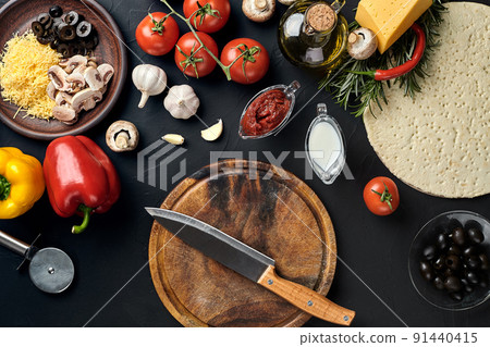 Cutting wooden board with traditional pizza preparation ingredients: cheese, tomatoes sauce, basil, olive oil, pepper, spices. Black texture table background Cutting wooden board with traditional pizza preparation ingredients: cheese, tomatoes sauce, basil, olive oil, pepper, spices. Black texture table background 91440415