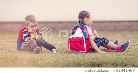 A boy and a girl quarreling and are sitting on the grass in the schoolyard back to back 91441407