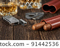 Two Cuban cigars, a cutter and a lighter in a leather case on an old brown table 91442536