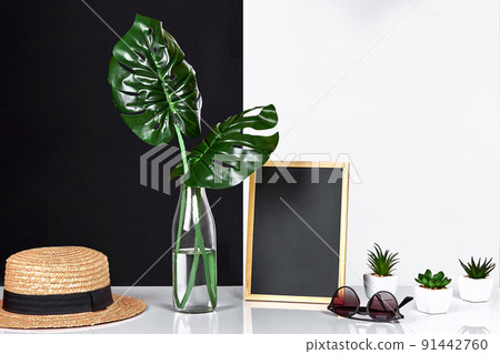 The stylish interior with mock up poster frame, leaves in glass bottle on table with black and white wall on background. The stylish interior with mock up poster frame, leaves in glass bottle on table with black and white wall on background. 91442760