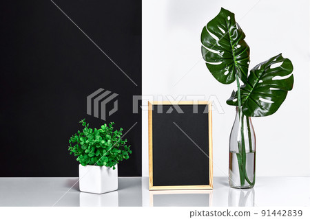 The stylish interior with mock up poster frame, leaves in glass bottle on table with black and white wall on background. The stylish interior with mock up poster frame, leaves in glass bottle on table with black and white wall on background. 91442839