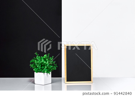Wooden frame with black place for text. Mock up. Stylish room interior. Green plant in a white pot on black-white wall background Wooden frame with black place for text. Mock up. Stylish room interior. Green plant in a white pot on black-white wall background 91442840