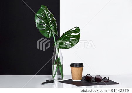 Hot coffee in brown paper cup and green leaves in glass bottle put on table with black and white wall on background 91442879