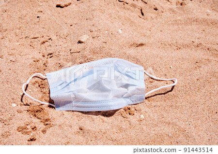 Blue medical mask lies on the sand on the beach Blue medical mask lies on the sand on the beach 91443514