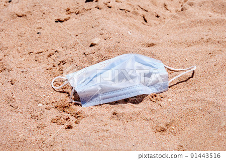 Medical mask on the sand of the beach as a reminder of the pandemic Medical mask on the sand of the beach as a reminder of the pandemic 91443516