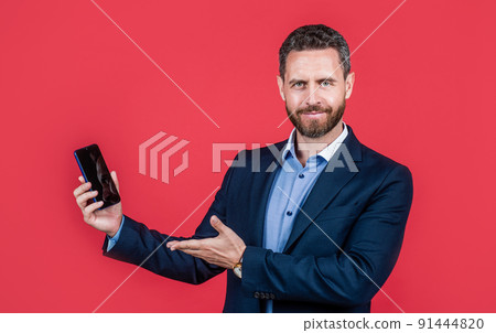 mature cheerful man in businesslike suit presenting product of smartphone, copy space, advert. 91444820
