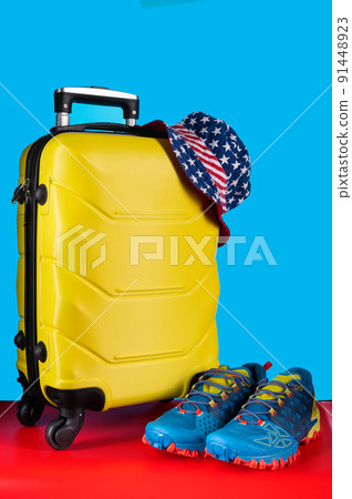 Travel luggage and sports shoes. Yellow suitcase and panama. Panama in the shape of the American flag. 91448923