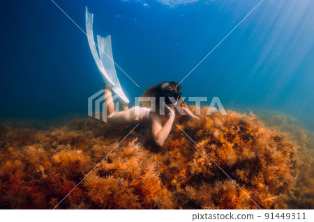 Young woman with diving mask and white fins posing and look at camera in underwater. Freediving and sunlight in blue ocean 91449311