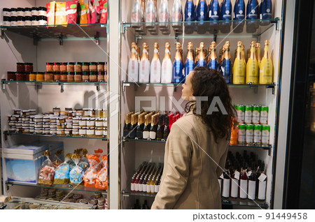 Rear view of brunette traveler woman looking at stalls with different food items and goods while shopping in duty free shop in international airport Rear view of brunette traveler woman looking at stalls with different food items and goods while shopping in duty free shop in international airport 91449458