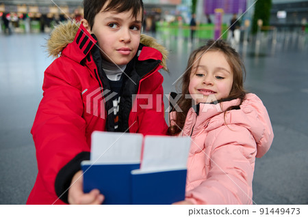Adorable kids siblings hold boarding pass and Identity document in hands while waiting for check-in flight in departure hall of international airport Adorable kids siblings hold boarding pass and Identity document in hands while waiting for check-in flight in departure hall of international airport 91449473