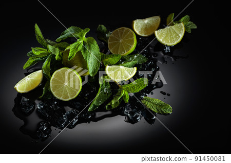 Slices of lime, mint leaves, and ice pieces on a wet black background. 91450081