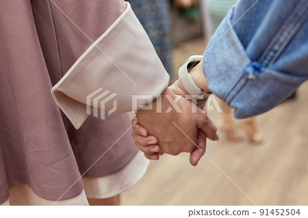 Close up of a woman's hand with two women sitting face to face and holding each other's hands. 91452504