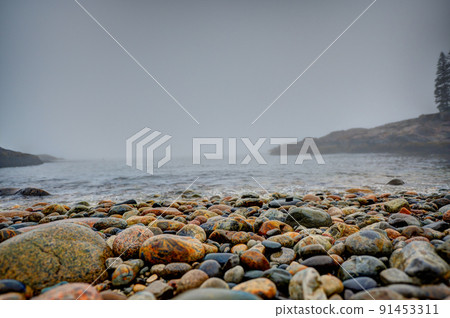 Multi-colored round rocks on Little Hunters Beach in Acadia National Park, Maine. Tide coming in as waves crash.  91453311