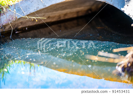 Oil sheen on contaminated storm water runoff coming out of a concrete culvert 91453431