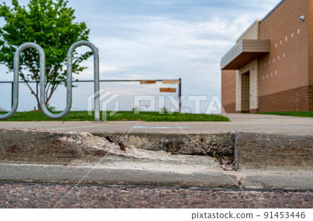 Broken sidewalk curb with exposed rebar and jagged edges that could cause a tripping hazard 91453446
