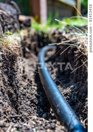Focus on a black 1 inch sprinkler plastic water line laid in a shallow trench 91453458