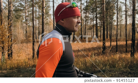 Training an athlete on the roller skaters. Biathlon ride on the roller skis with ski poles, in the helmet. Autumn workout. Roller sport. The athlete goes and holds sports equipment in his hand. 91455127