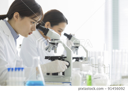 一個穿白大褂的女人透過顯微鏡看 91456092