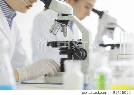 A woman in a white coat looking through a microscope 91456093