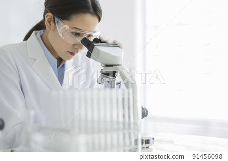 一個穿白大褂的女人透過顯微鏡看 91456098