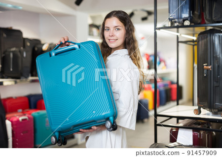 Satisfied girl in a shop, holding a travel suitcase Satisfied girl in a shop, holding a travel suitcase 91457909