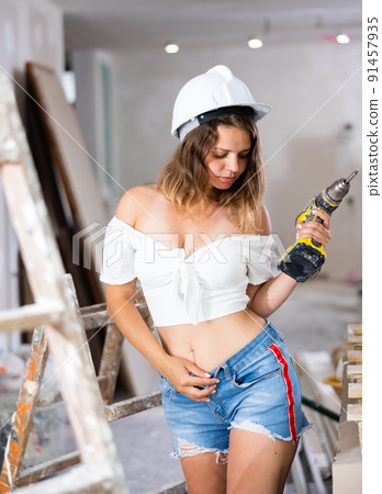 Pretty woman in a white blouse and short shorts poses playfully with a screwdriver in renovated room Pretty woman in a white blouse and short shorts poses playfully with a screwdriver in renovated room 91457935